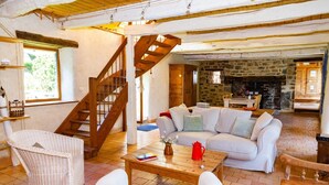A cozy living room with a wooden staircase, a stone fireplace, and a white sofa.