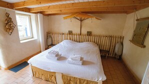A bedroom with a wooden bed, a window with curtains, a radiator, and a wooden ceiling.