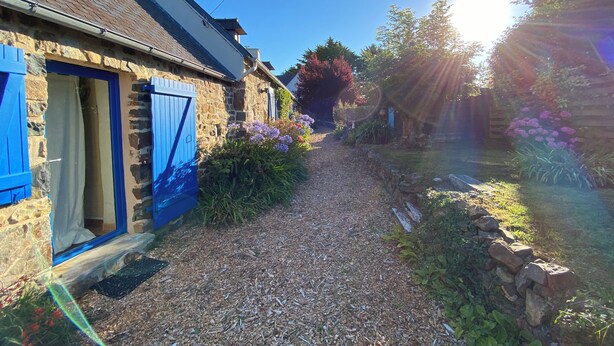 A narrow gravel path leading to a stone house with blue shutters and a door.