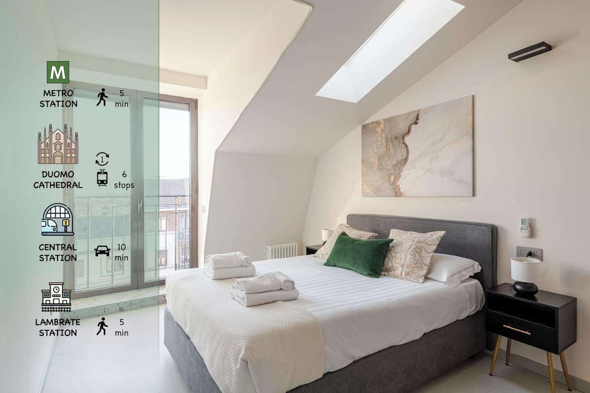 A modern bedroom with a large bed, a nightstand, a painting, and a view of a metro station.