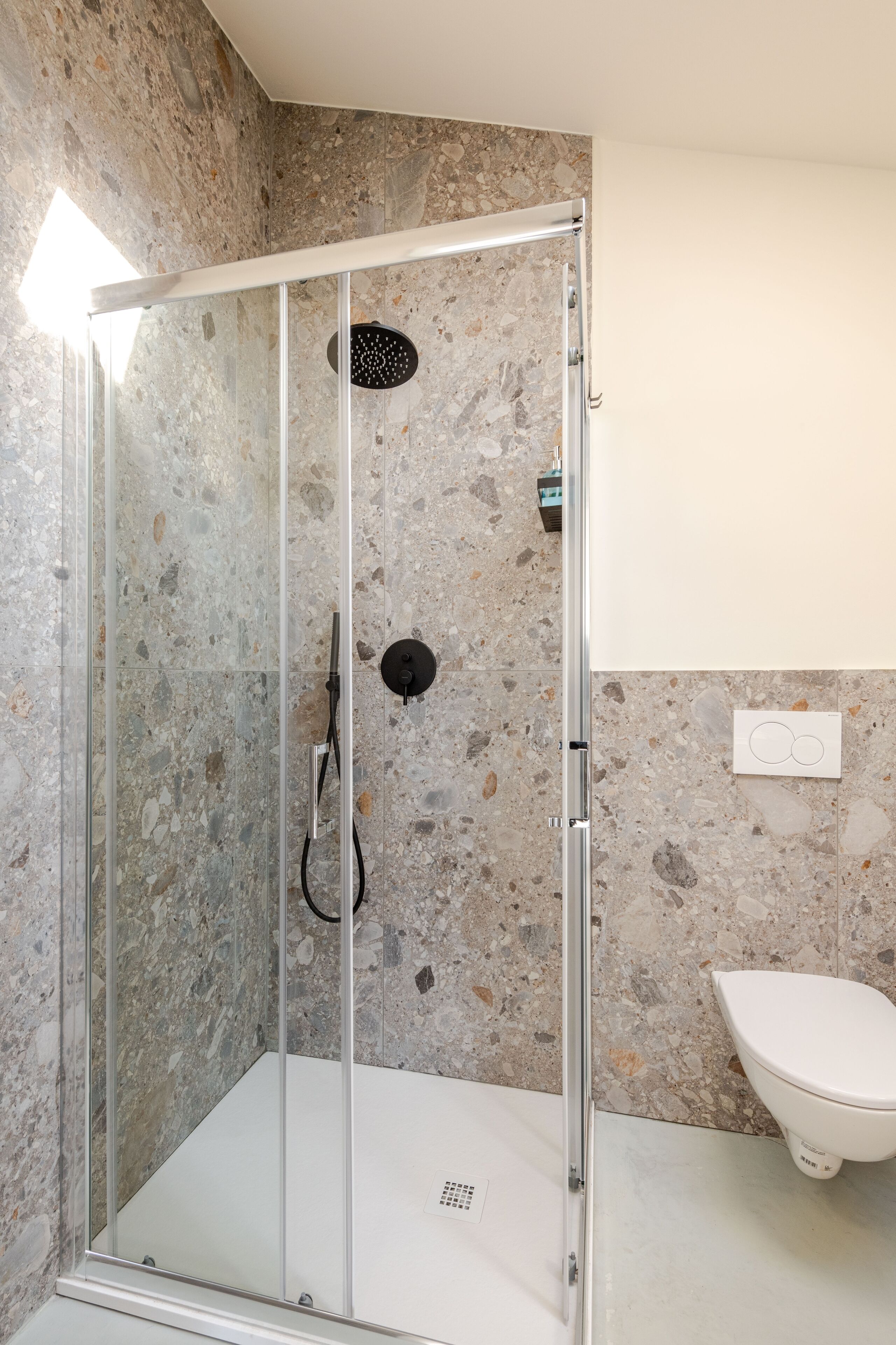 A glass-enclosed shower with a stone-tiled wall, a white toilet, and a visible electrical outlet.