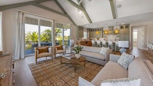 A spacious living area with a sofa, chairs, and a coffee table. There is a balcony with large windows and a view of palm trees. - Elegance~Gorgeous! Arcade!~ Heated pool/spa~North End! (Anna Maria)