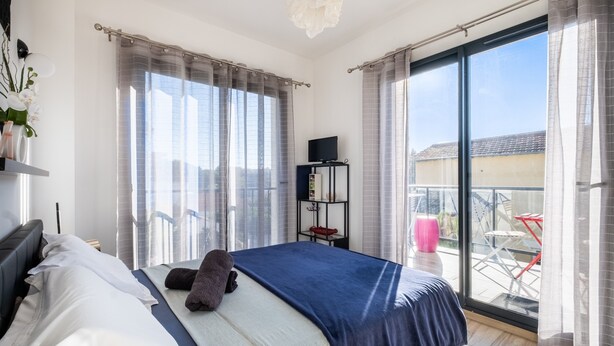 Een slaapkamer met een bed, een televisie, een plank en een balkon met stoelen.