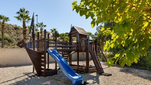 Un parque infantil con un tobogán, estructuras para escalar y un pequeño refugio.