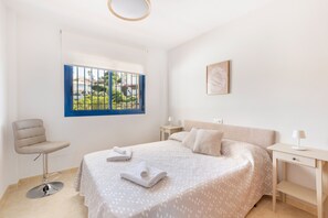 Ein Schlafzimmer mit Bett, Stuhl, Schreibtisch, Fenster mit Aussicht und einem Wandbild.