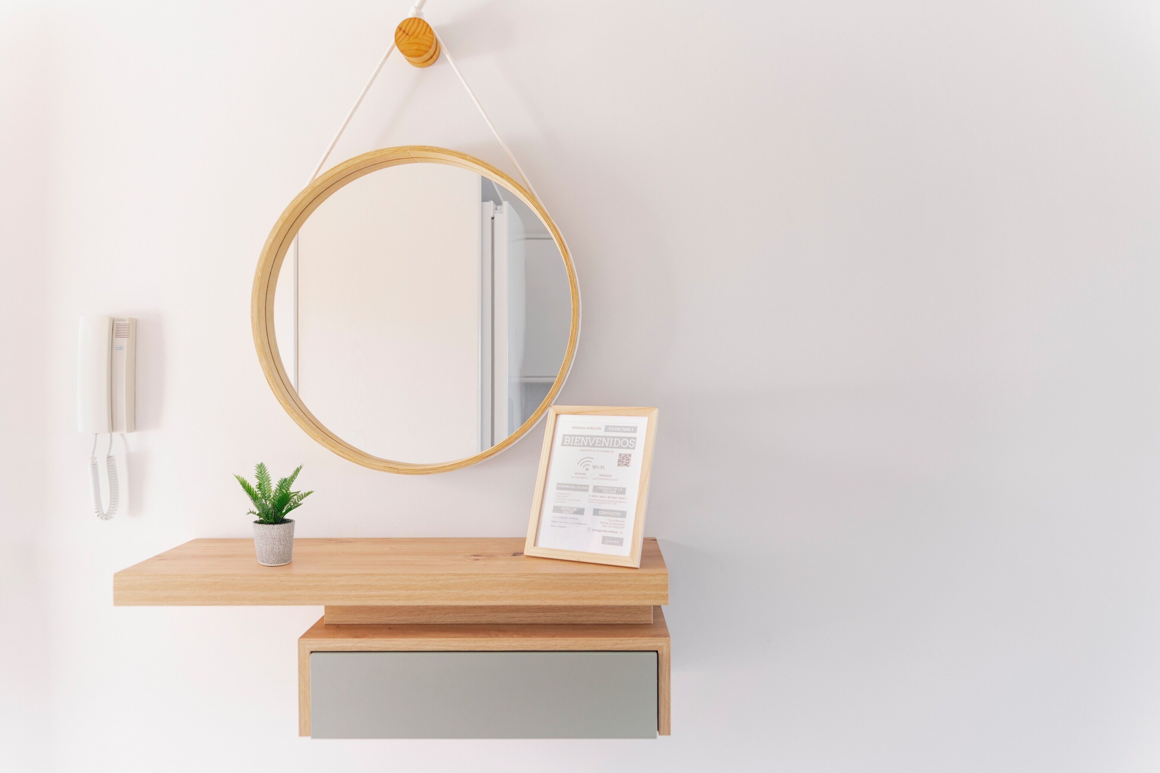 A wooden reception desk with a round mirror, a small potted plant, a framed welcome sign, and a telephone.