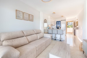 Ein modernes Wohnzimmer mit einem beigefarbenen Sofa, einem Holztisch und einer Küche im Hintergrund.
