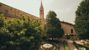 A courtyard with a brick building, a tower, and a circular flower bed. - Suite Seta (Castelvetro di Modena)
