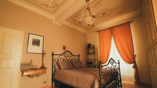 A bedroom with a four-poster bed, a chandelier, a bookshelf, and a large window with curtains. - Suite Seta (Castelvetro di Modena)