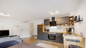 Eine moderne Küche mit integrierten Geräten, ein Essbereich mit Tisch und Sofa sowie eine kleine Sitzecke mit einem Sessel.