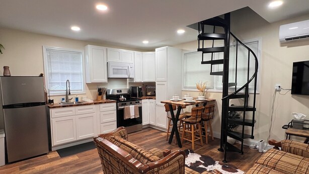 Cocina moderna con armarios blancos, un refrigerador de acero inoxidable y una escalera espiral negra que lleva a una habitación superior.