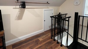 Una habitación con suelo de madera, una puerta, una barandilla de metal negro y un reloj en la pared.
