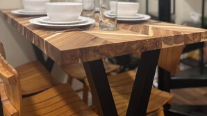 Una mesa de comedor con platos y tazones blancos, un vaso y un tenedor. Se ven sillas de madera y una escalera de metal negro al fondo.