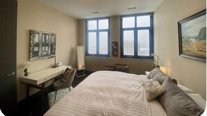 Une chambre à coucher avec un lit, un bureau, une chaise et de grandes fenêtres.