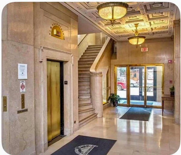 Un vestíbulo con suelo de mármol, una escalera y una zona de recepción con puerta de cristal.