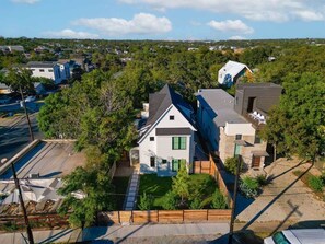 Un quartier résidentiel avec une maison blanche dotée d’un toit en pente, de volets verts et d’un petit jardin à l’avant.