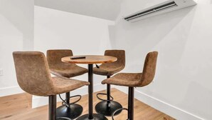 Ein Eckzimmer mit einem runden Holztisch und vier bequemen, braunen Sesseln. Eine Klimaanlage ist an der Wand angebracht.