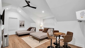 Ein modernes Schlafzimmer im Loft-Stil mit zwei Betten, einem Essbereich und einem Deckenventilator.