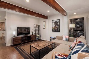 A modern living room with a television, sofa, coffee table, and a built-in washer and dryer.