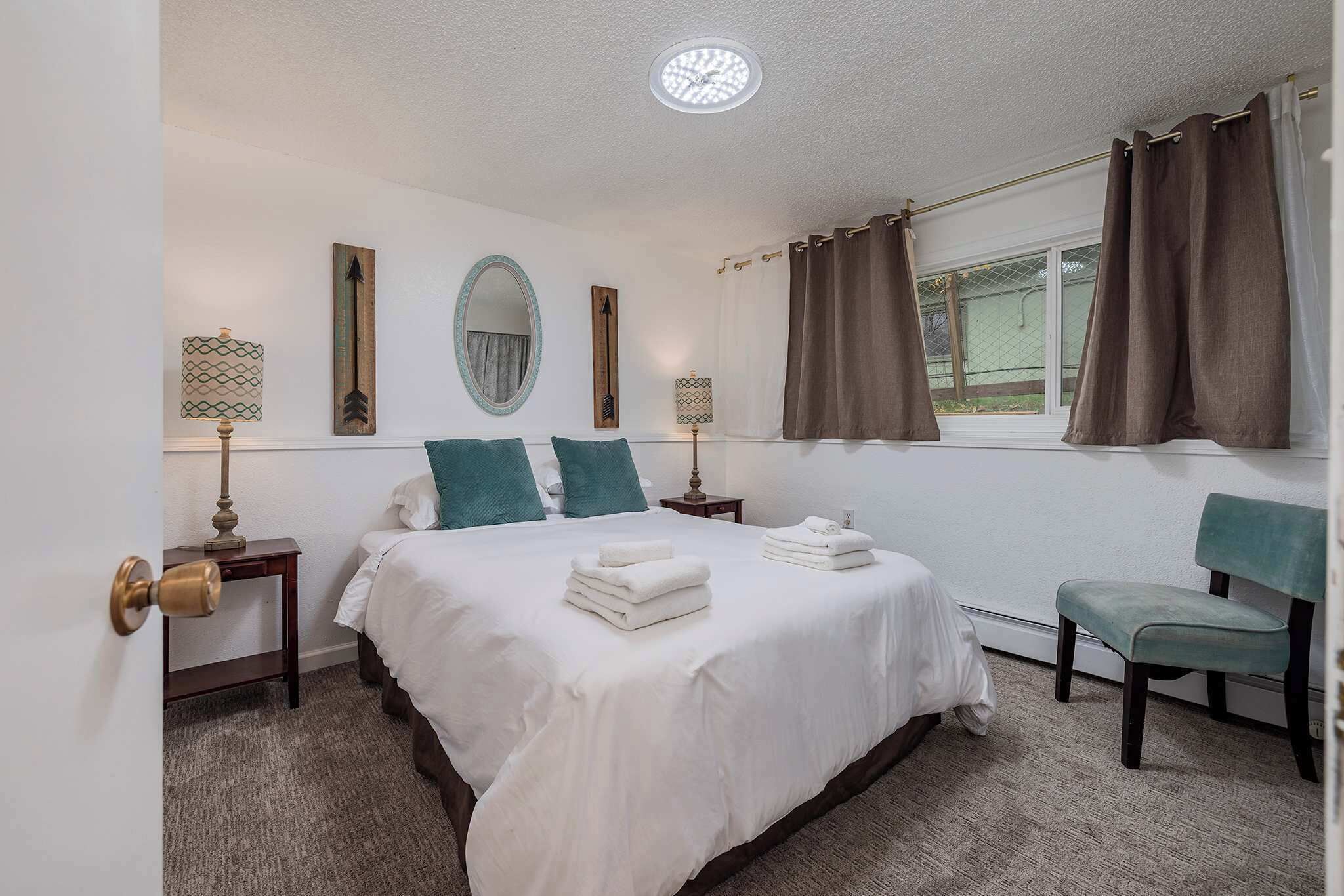 Een slaapkamer met een bed, twee nachtkastjes, een stoel, een raam met gordijnen en wanddecoratie.