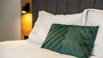 A bed with white bedding and a green pillow, a grey headboard, and a wall-mounted light fixture.