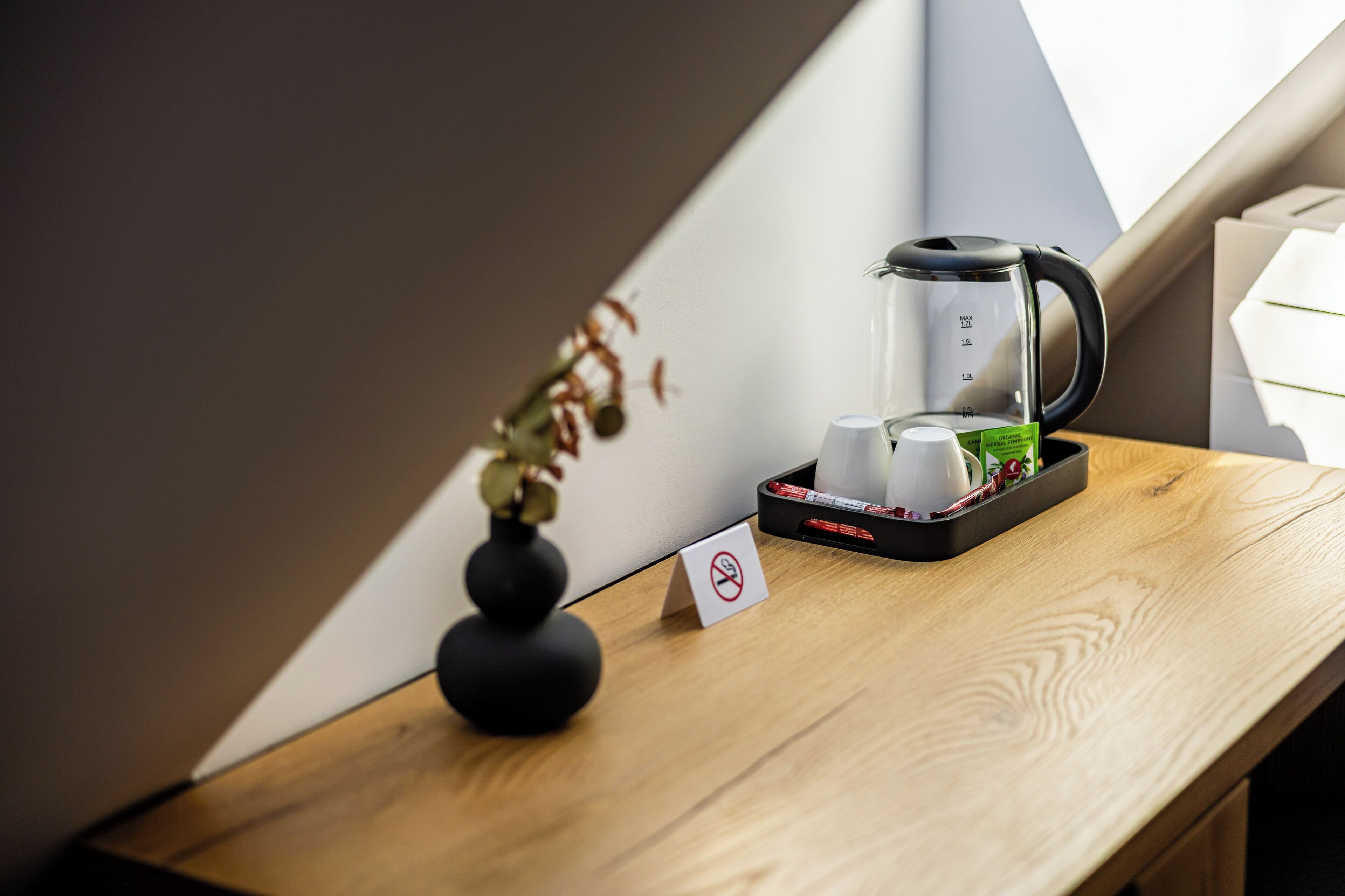 A wooden table with a coffee maker, a vase with dried flowers, and a no-smoking sign.