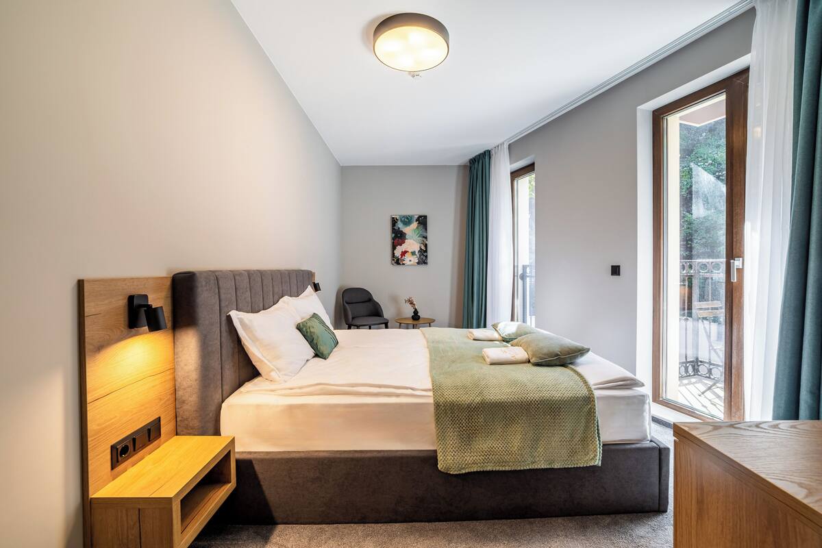 A modern bedroom with a large bed, bedside tables, a desk, and a view of the outdoors.