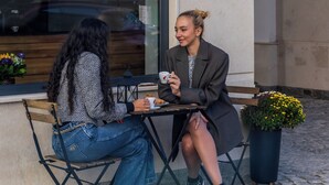 Two people seated at an outdoor table with a city view, a sign for "ACACAO HOTEL" above, and a potted plant nearby. - Acacia Boutique Hotel (Sofia)