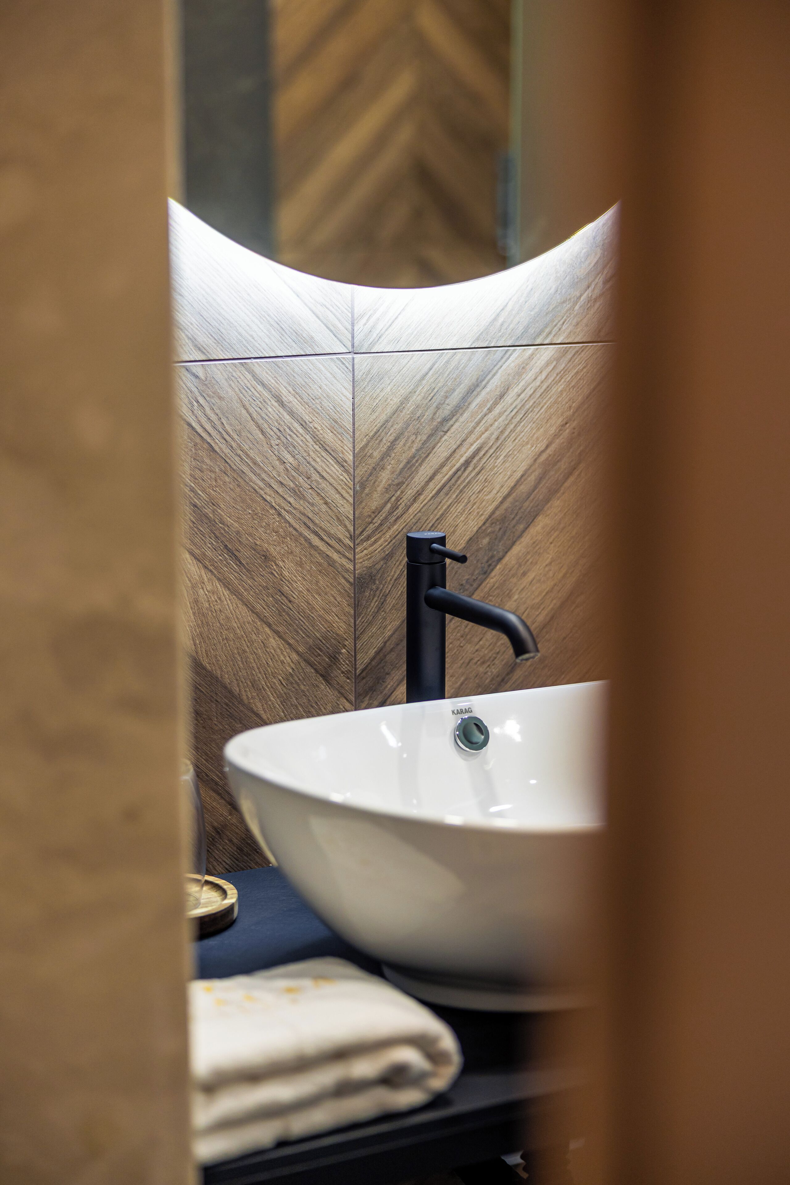A modern bathroom with a white sink, black faucet, and a wooden herringbone-patterned wall.