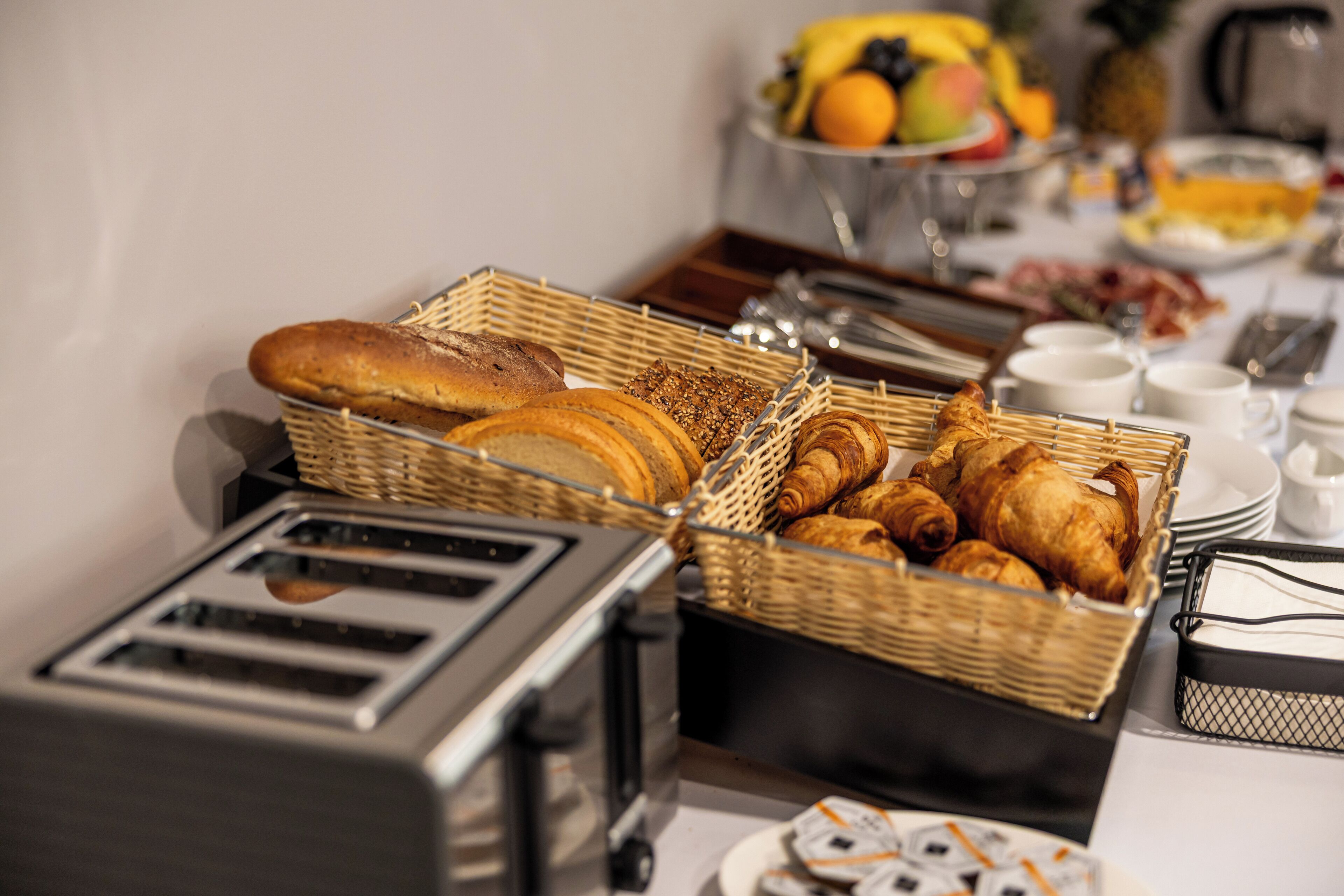 A breakfast buffet with various breads, pastries, and fruits.