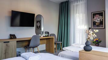 A hotel room with two beds, a desk with a chair, a TV, a coffee maker, and a vase with flowers.