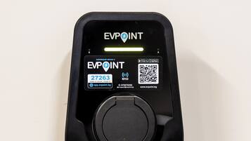 Una estación de carga EVPOINT negra con un código QR, iconos de la tienda de aplicaciones y un identificador de cargador.