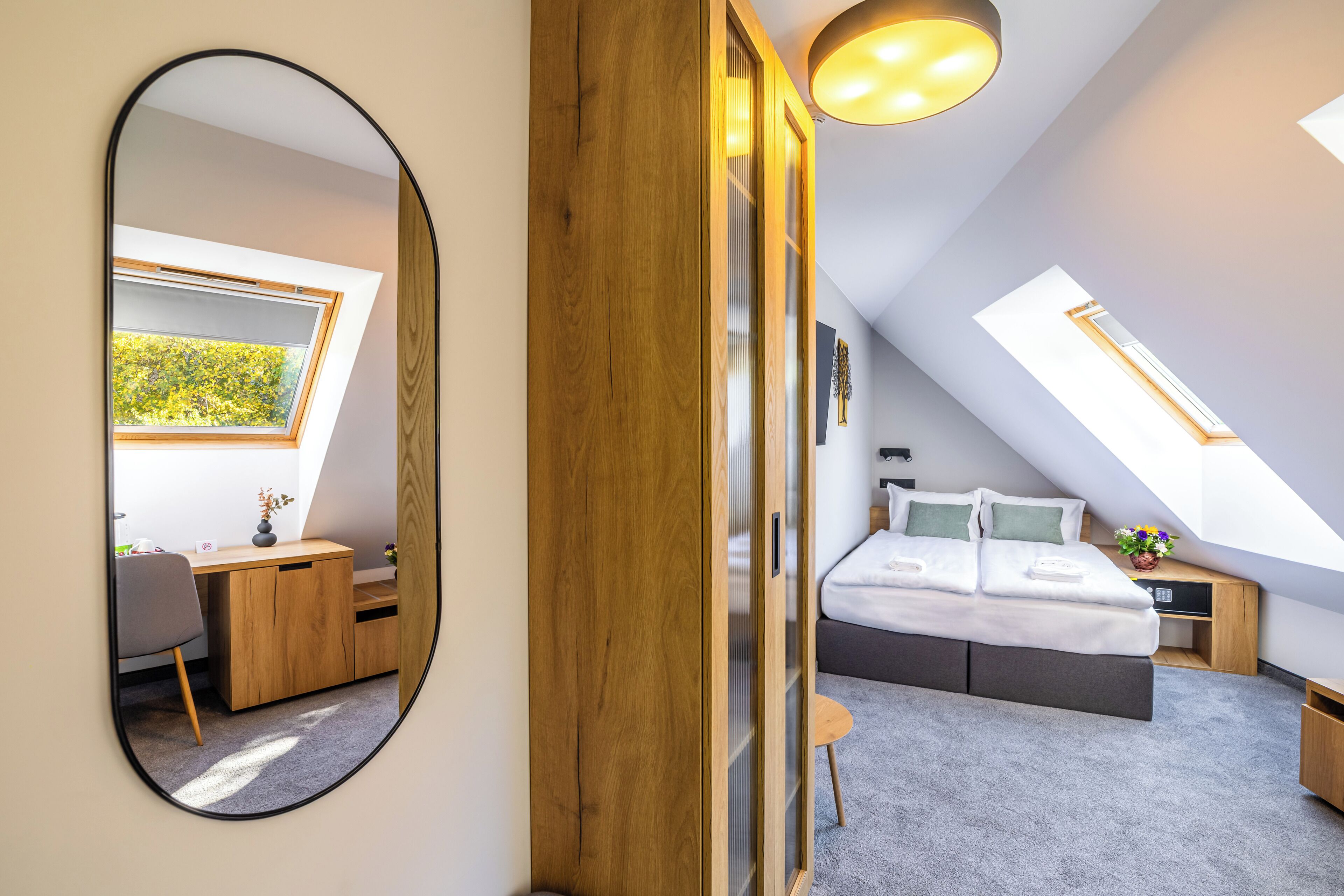 A bedroom with a skylight, a bed, a desk, and a chair.