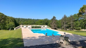 A swimming pool with a stone deck, surrounded by a stone wall and a grassy area with trees. - Château Ecrin de lumiere (Campsegret)