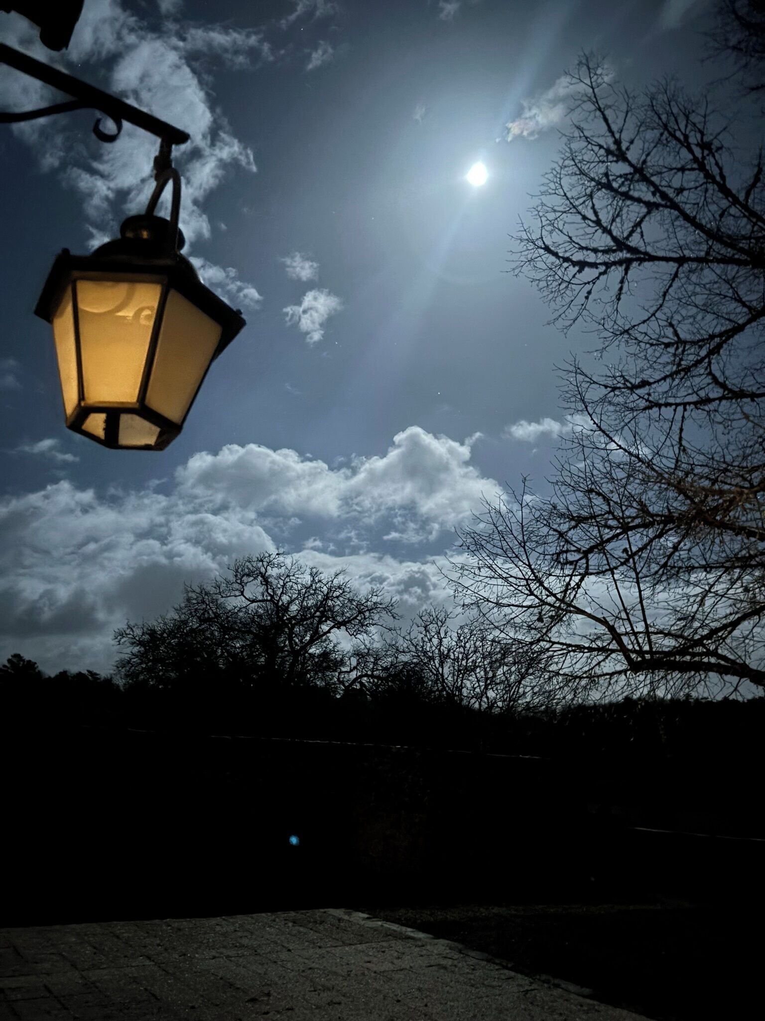A street lamp against a cloudy sky with a bright moon.