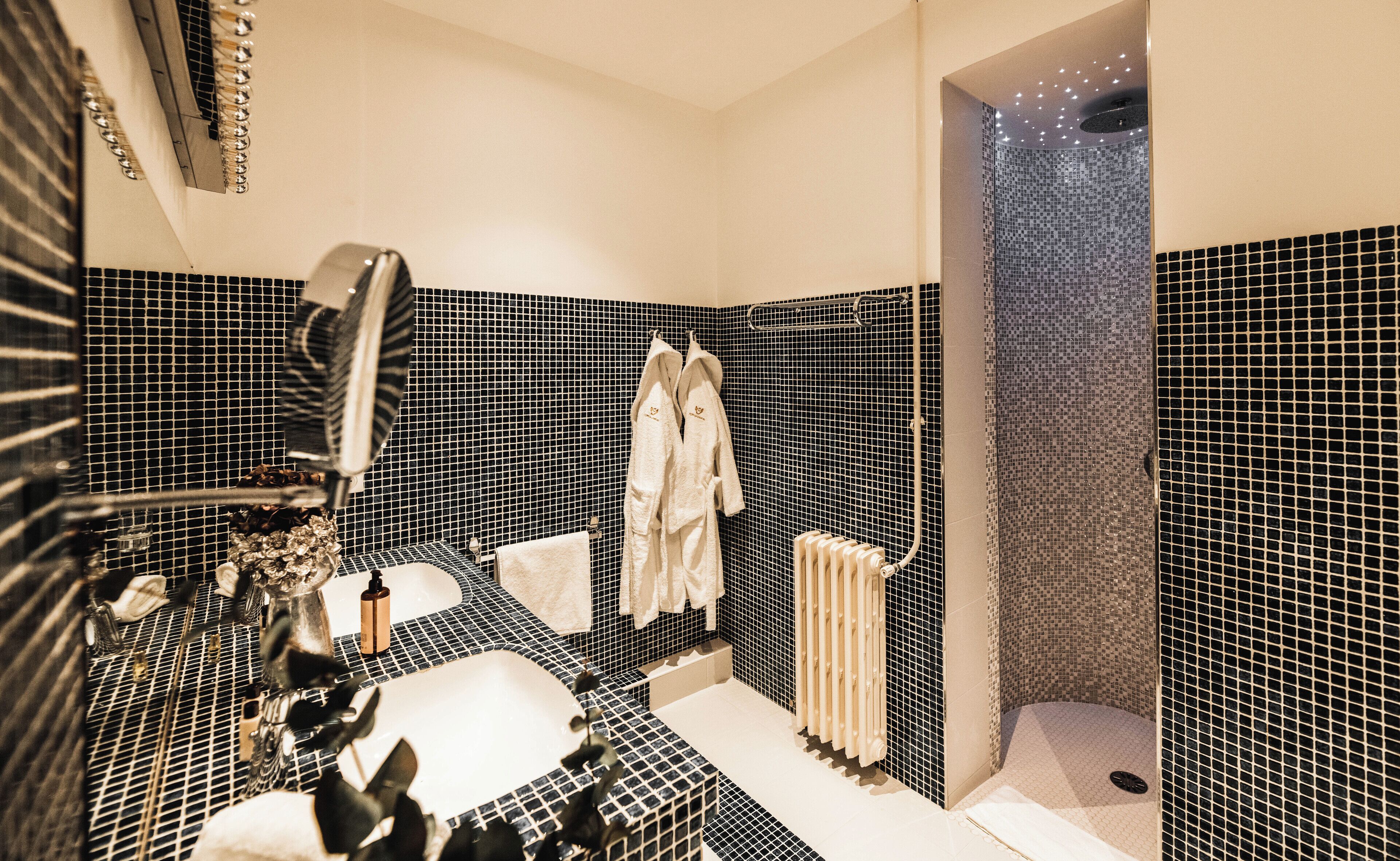 A bathroom with a black and white tiled wall, a bathtub, a shower area, and a towel rack with two towels.