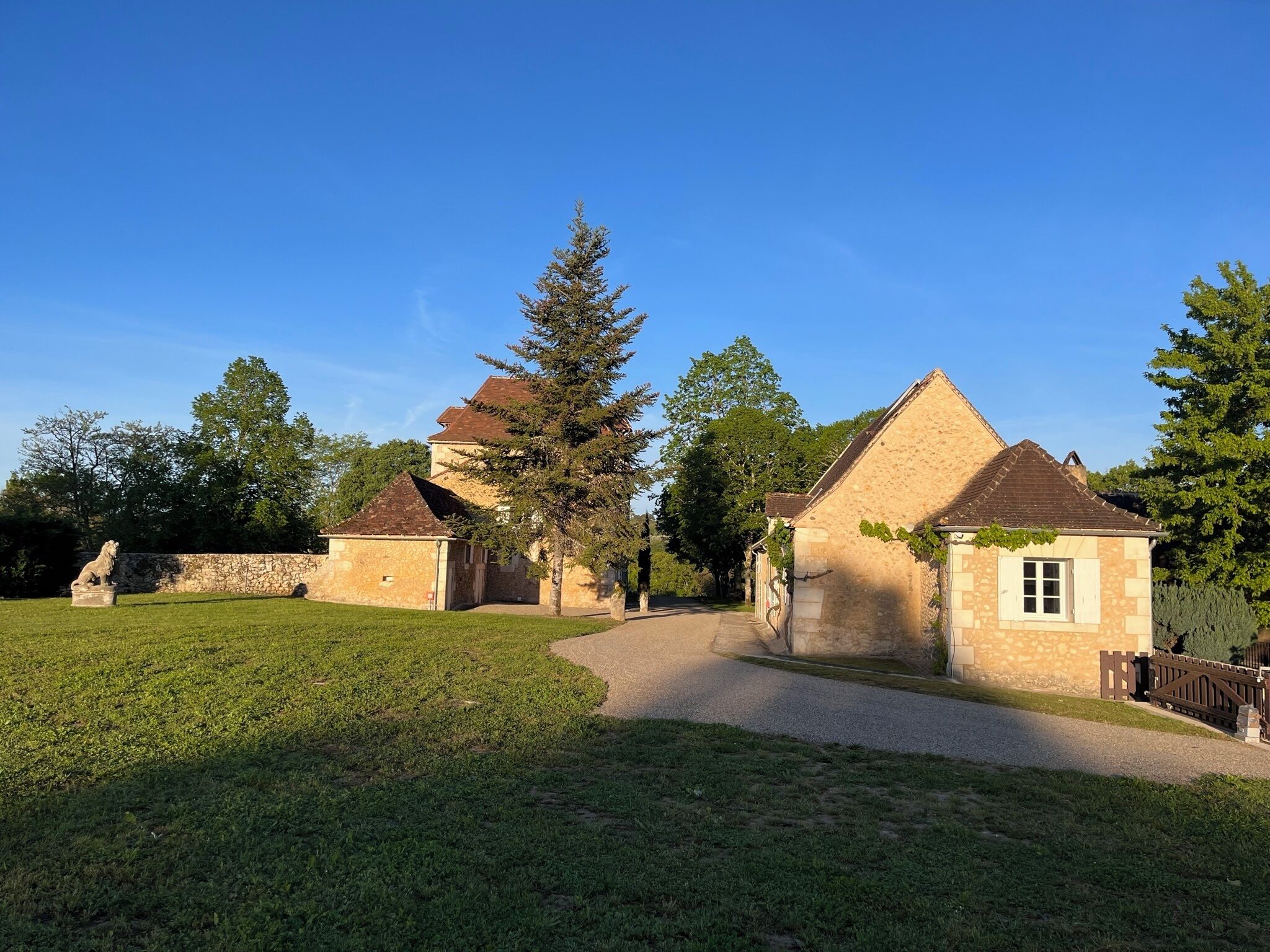 Un bâtiment en pierre avec un toit en tuiles, une pelouse verdoyante et une statue.