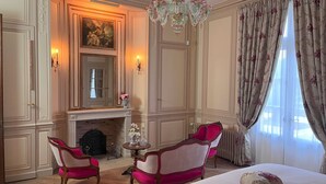 A classic room with a fireplace, two armchairs, a chandelier, and a large bed with floral pillows. - Château Ecrin de lumiere (Campsegret)