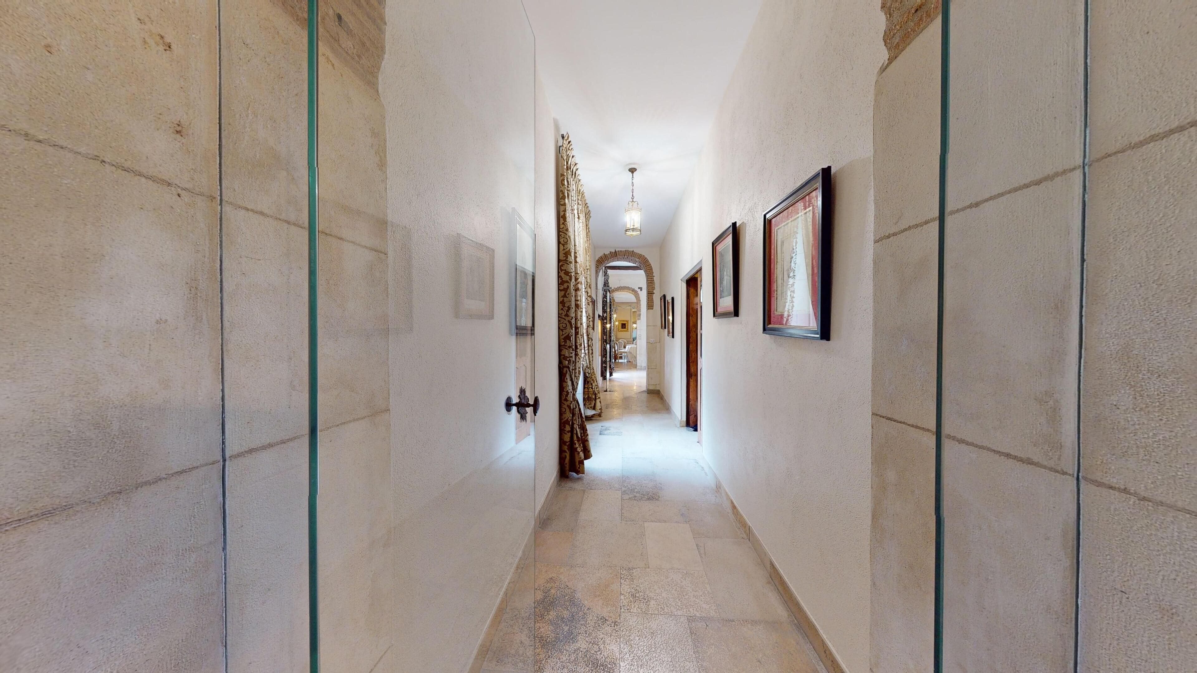 A hallway with tiled walls, a tiled floor, a door with a glass panel, and a hanging light fixture.