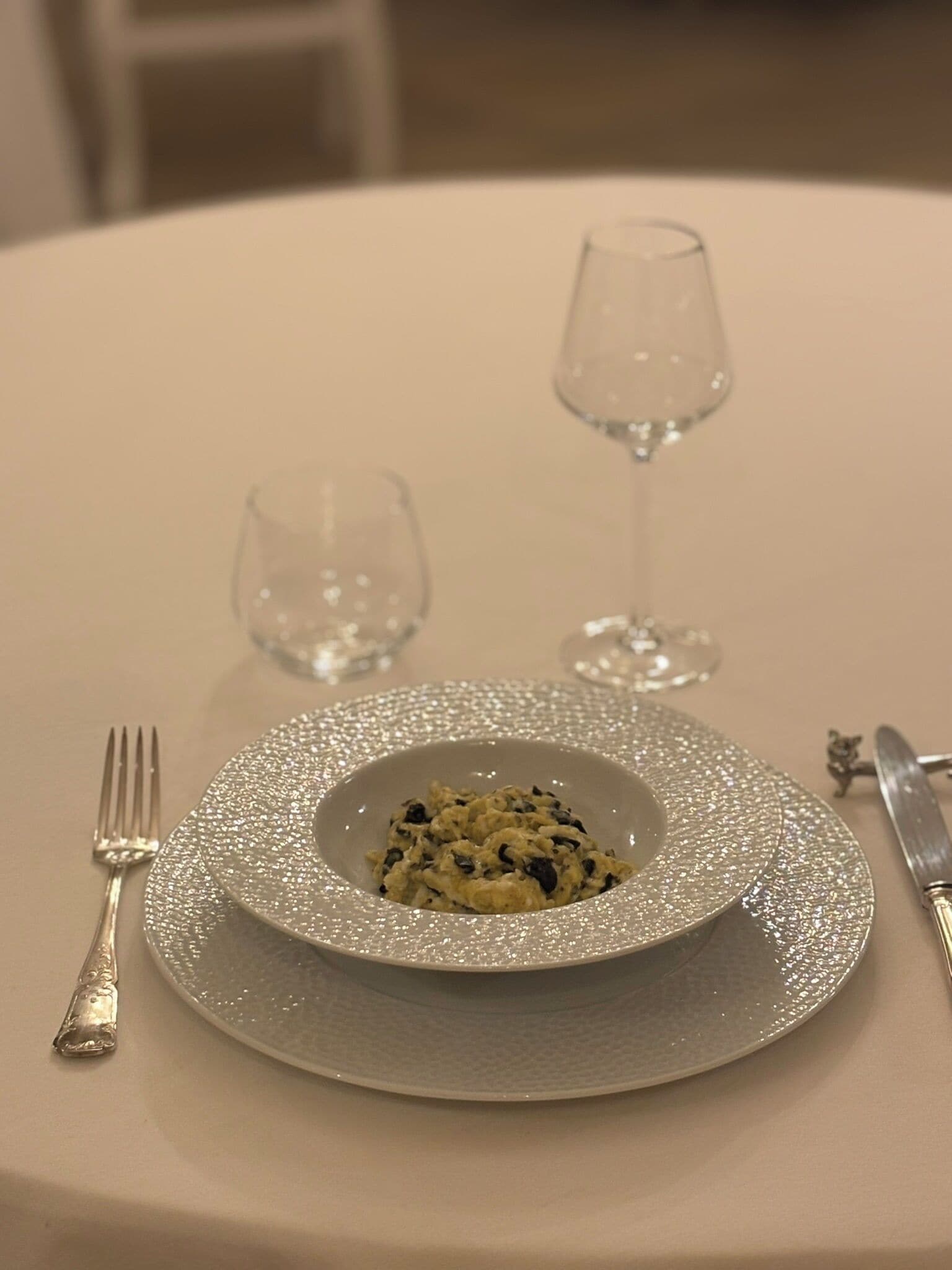 Una mesa con un plato de comida, un tenedor, un cuchillo y dos copas de vino.