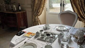 A dining table set with plates, cutlery, glasses, and a variety of food items, with a window and curtains in the background.