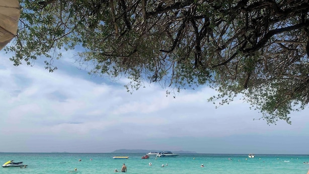 Ein Strand mit klarem türkisblauem Wasser, Booten und badenden Personen.
