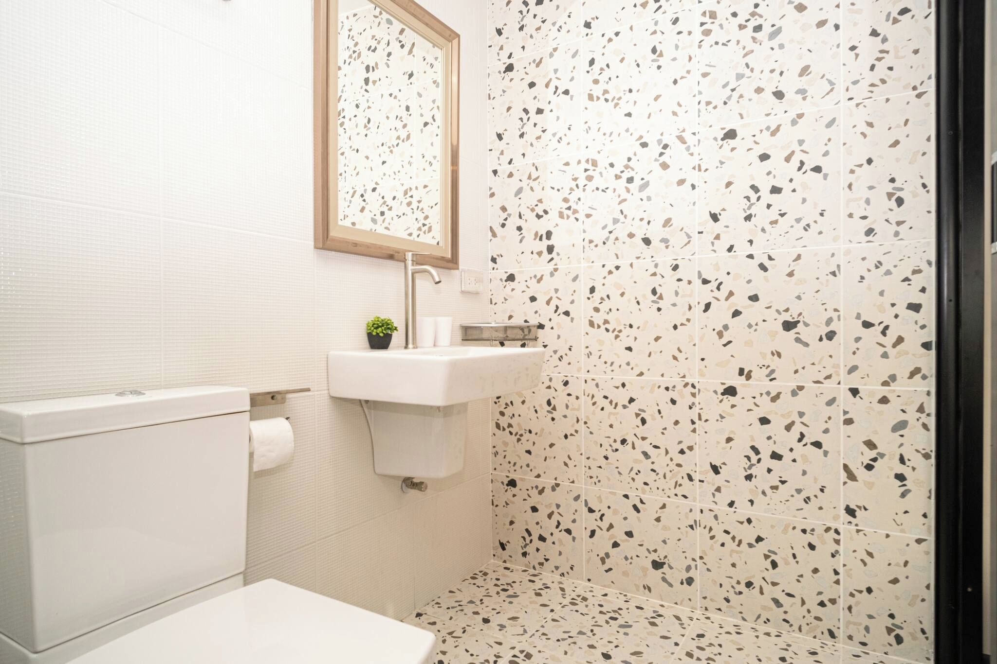 Ein Badezimmer mit einer weißen Toilette, einem Waschbecken mit Spiegel darüber und einer Wand mit unregelmäßig gemusterten Fliesen.