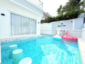 A swimming pool with inflatable toys, a white building with a name sign, and a clear sky.