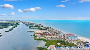 Vue aérienne d’un complexe hôtelier situé sur la côte, comprenant plusieurs bâtiments, un port de plaisance et une plage.