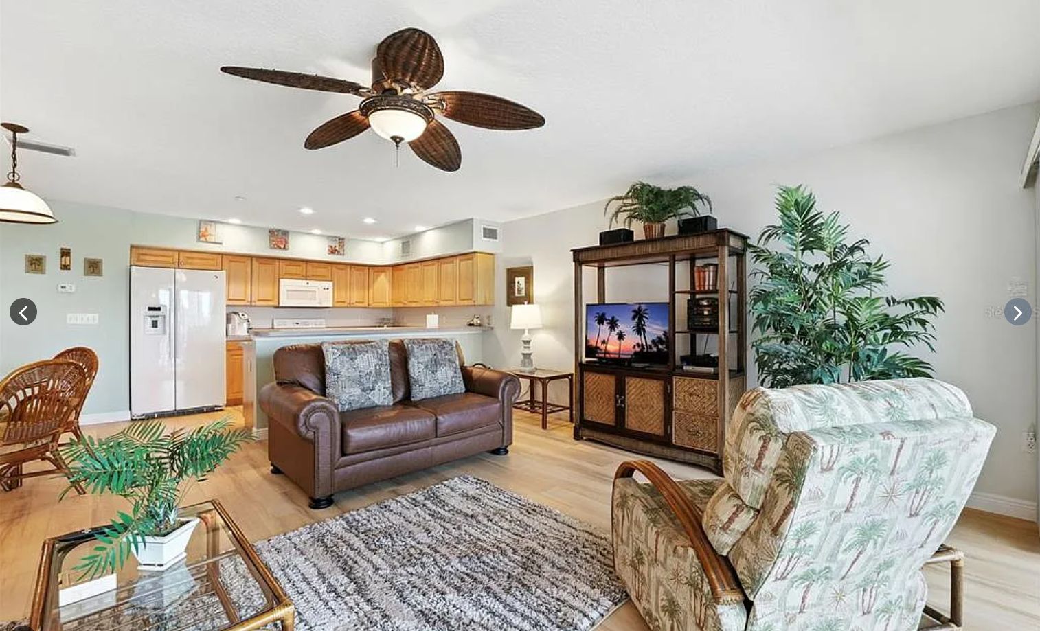 Ein Wohnzimmer mit einem braunen Ledersofa, einem gemusterten Sessel, einem Couchtisch und einem Fernseher auf einer Holzkommode.