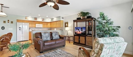 A living room with a brown leather sofa, a patterned armchair, a coffee table, and a TV on a wooden cabinet.