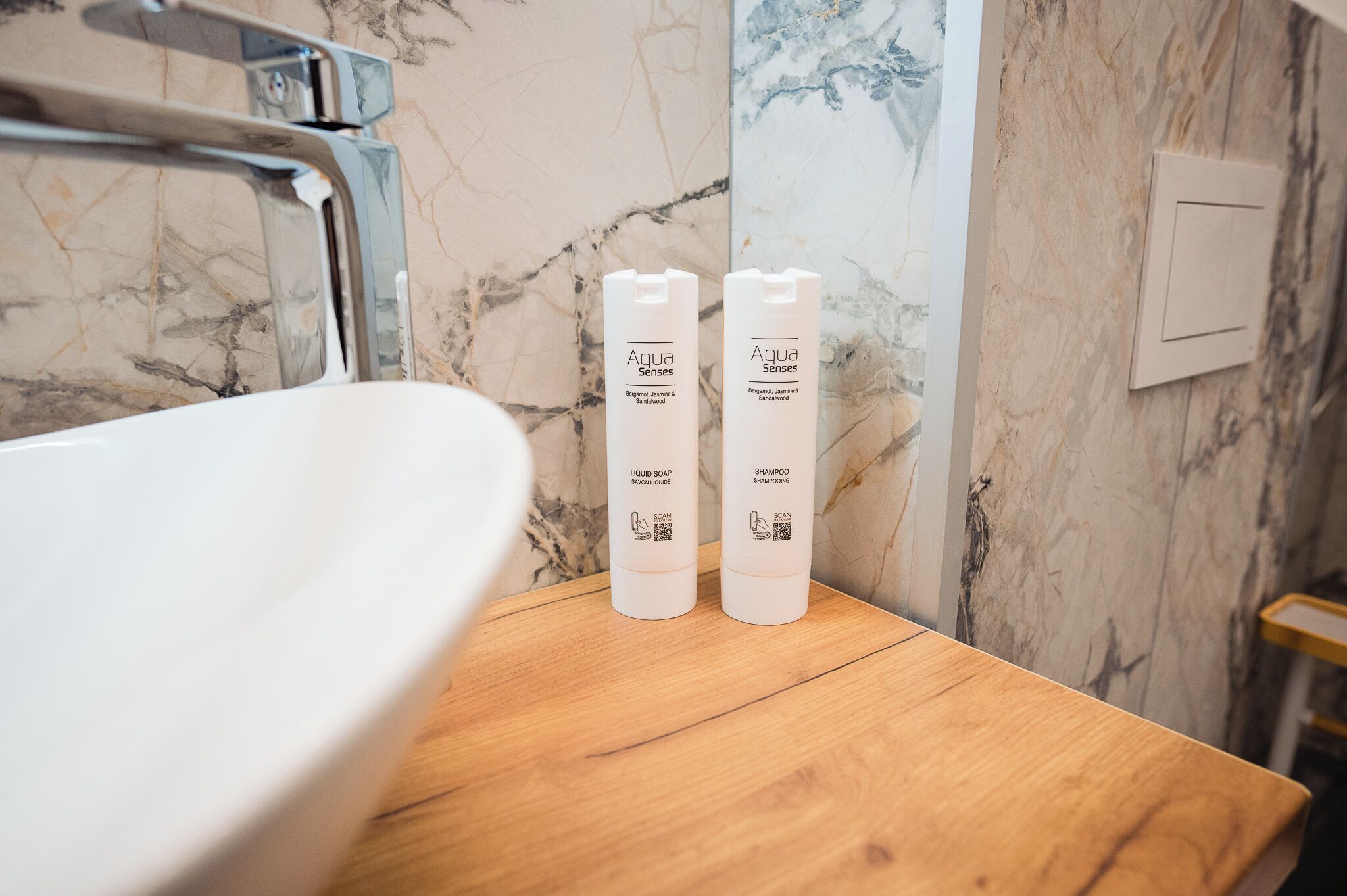 Un baño con pared de mármol, encimera de madera y dos botellas de jabón líquido y champú Aqua Senses.