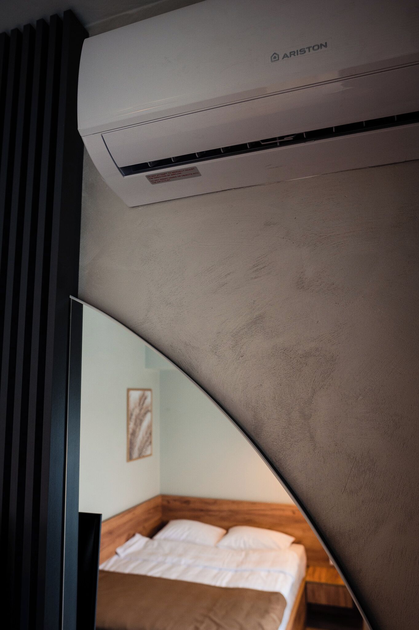 Una habitación moderna con cama, aire acondicionado instalado y una vista parcial de una pared con un cuadro enmarcado.