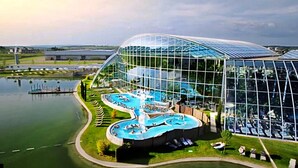 A modern building with a glass facade, a pool area with multiple water features, and a surrounding landscape. - FLY & STAY AT GEORGE'S (Otopeni)